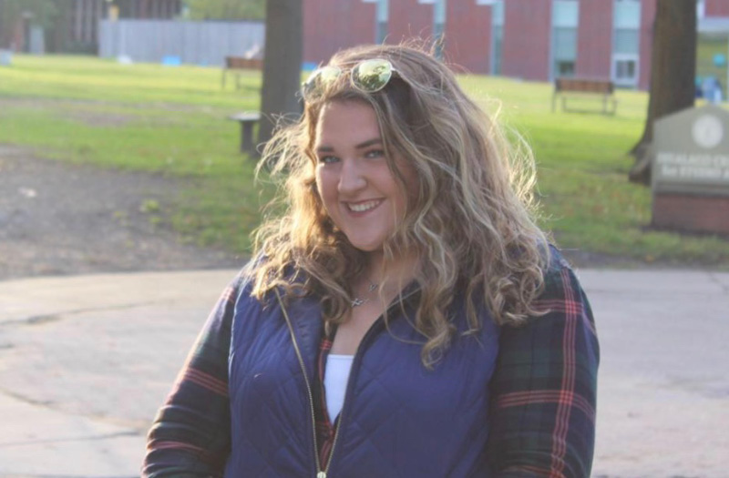 A young woman in a vest and flannel shirt.